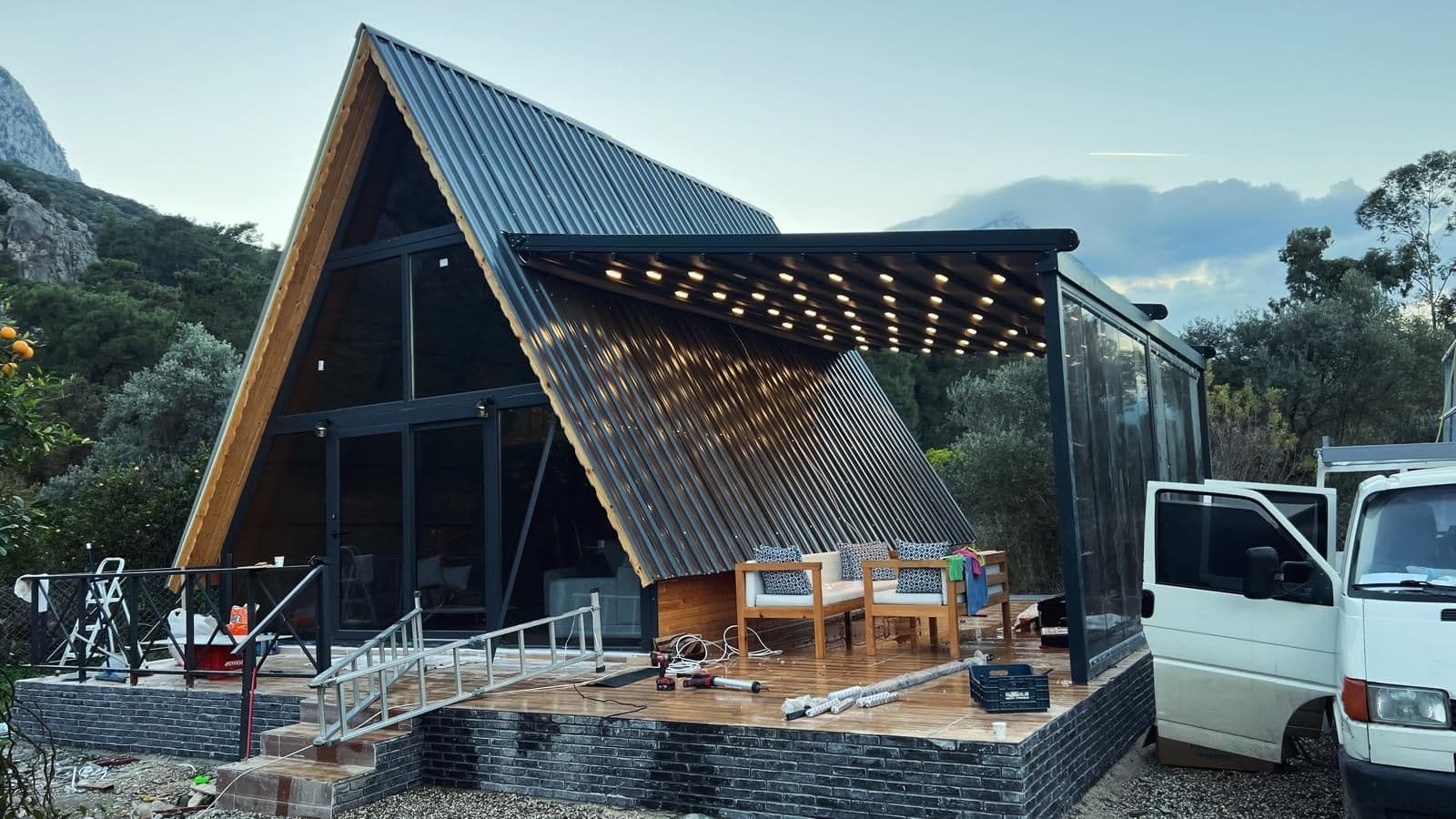 A çatılı bungalov terasına uygulanmış motorlu pergola tente, akşam saatinde LED aydınlatma yanıyor.