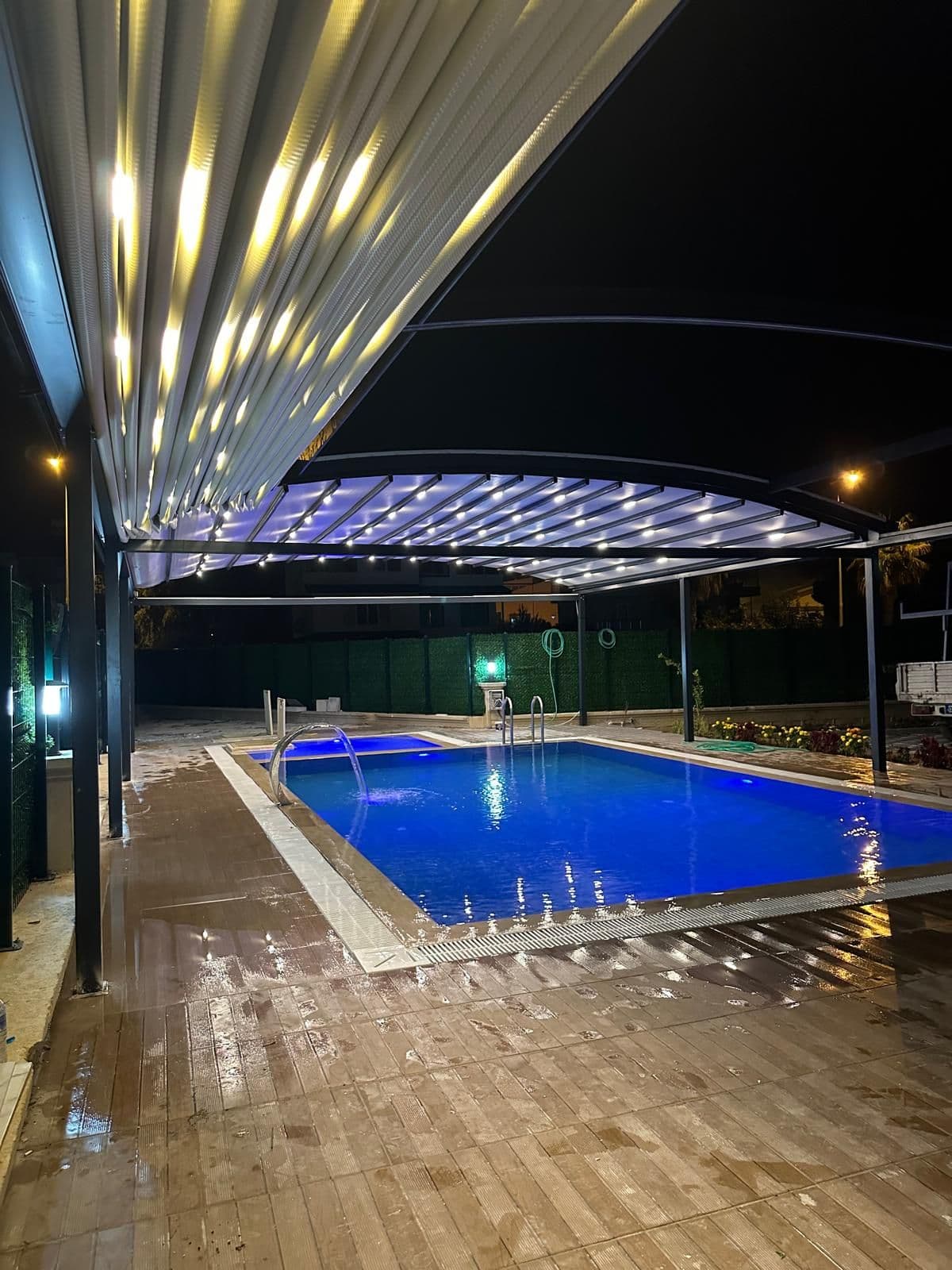 Havuz üzerine kurulmuş motorlu pergola tente; gece LED aydınlatması yanıyor.