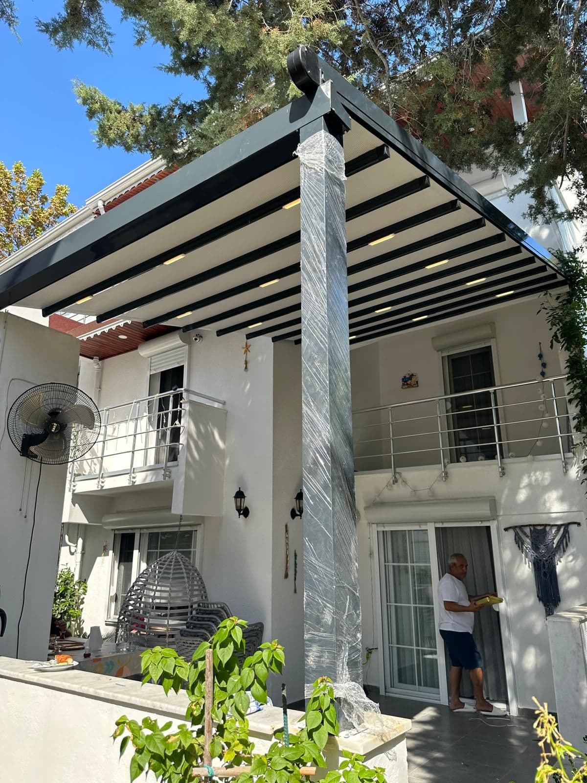 Villa cephesine monte edilmiş antrasit motorlu pergola tente; kumaş açık konumda.