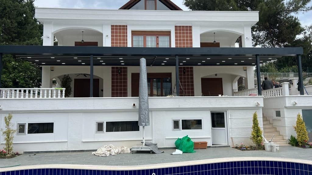 Villa cephesi boyunca uzanan antrasit renkli pergola sistemi, önünde havuz.
